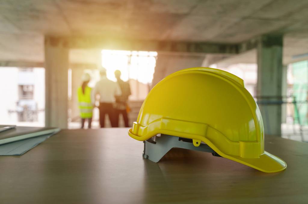 Yellow Safety Helmet On Workplace Desk With Construction Worker